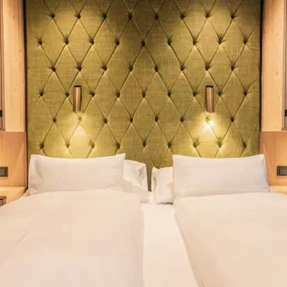 Modernes Hotelzimmer mit Doppelbett, grünem Polsterkopfteil und Holznachttischen